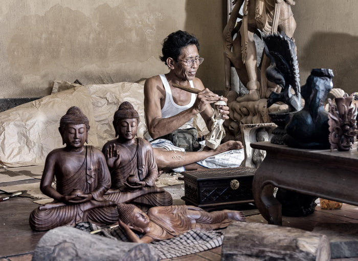 Ein Mann schnitzt auf Bali einen Buddha aus Holz